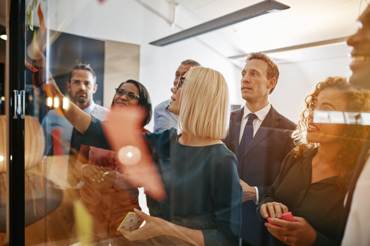 Eine Gruppe von Fachleuten bei einer Employer Branding Agentur arbeitet an einer Glaswand, um Strategien zur Stärkung der Arbeitgebermarke zu entwickeln.