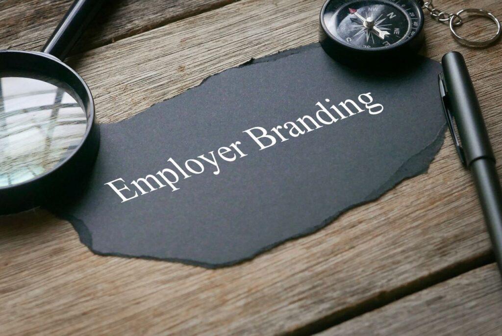 Nahaufnahme eines Employer Branding Konzepts auf schwarzem Papier, umgeben von Lupe, Kompass und Stift – symbolisch für die strategische Ausrichtung einer Employer Branding Agentur.