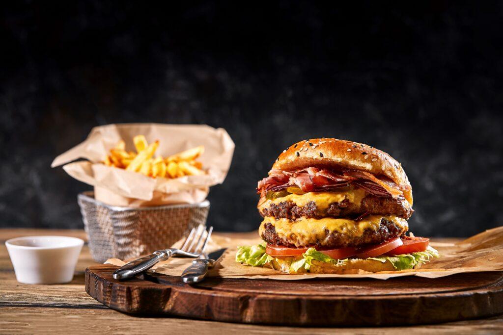 Cheeseburger auf einem Holzbrett, daneben eine kleine Schale Pommes