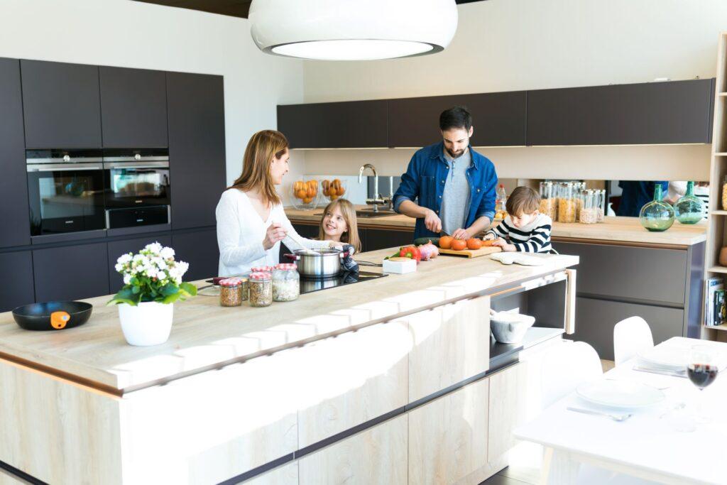 Familie beim gemeinsamen Kochen in moderner offener Kueche mit Kochinsel und Einbaugeraeten